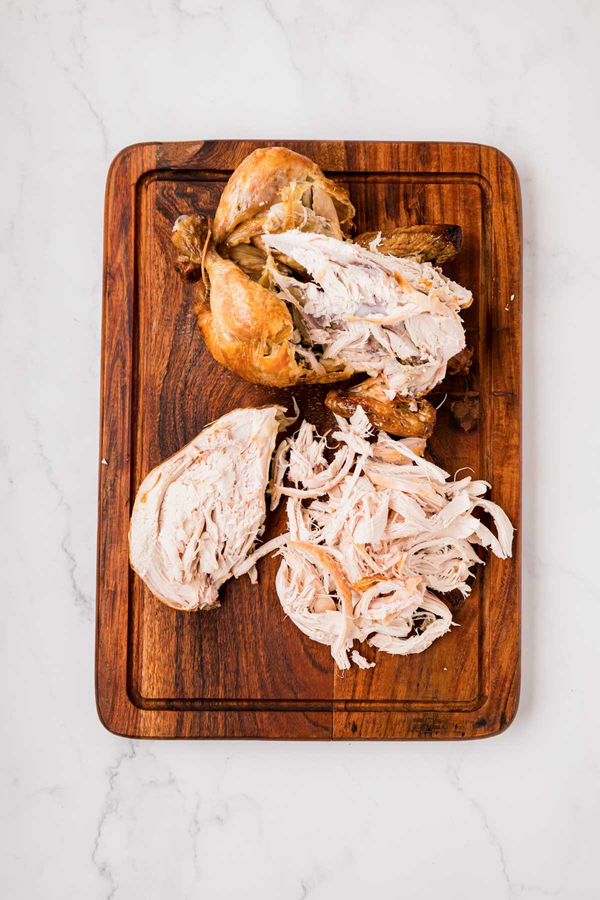 A rotisserie chicken on a cutting board with the breast meat removed and shredded.