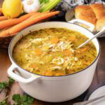 A white dutch oven filled with rotisserie chicken noodle soup.