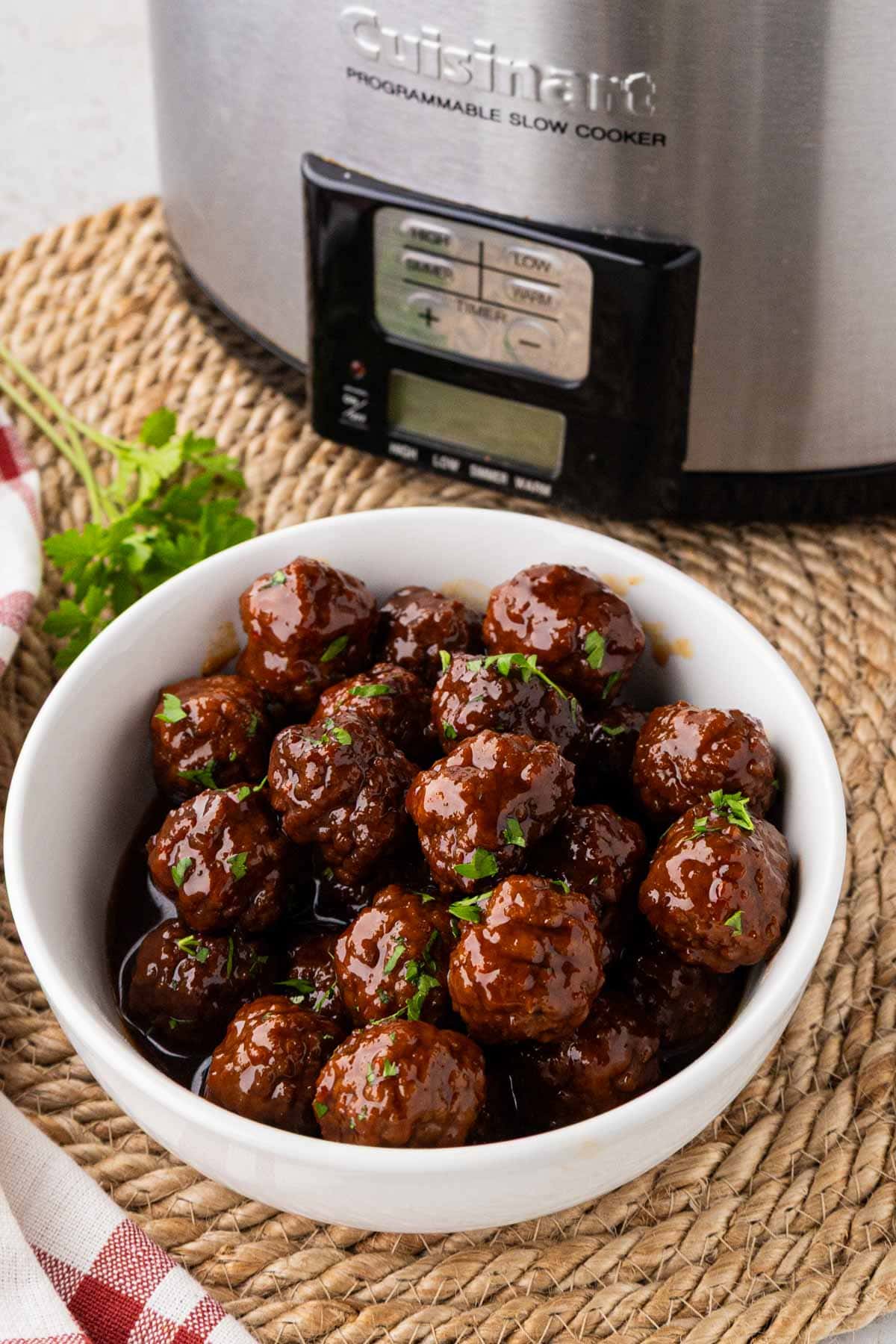 A white bowl filled with strawberry jalapeno pepper jelly meatballs with a crock pot in the background.