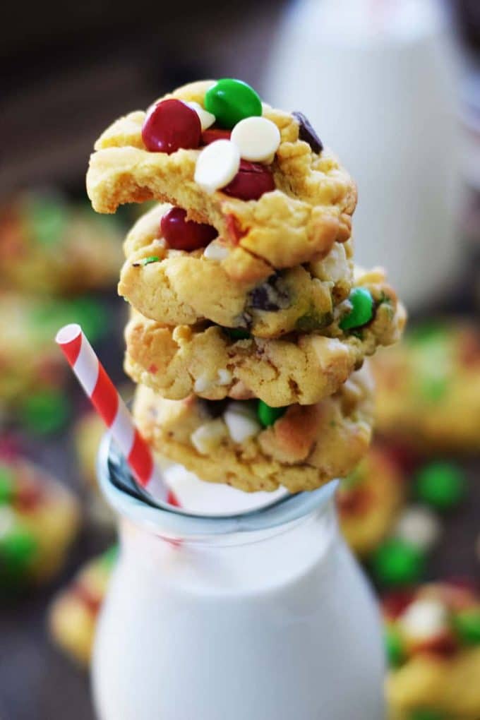 a stack of santa\'s chocolate chip cookies on top of a glass jar of milk with a red and white straw 