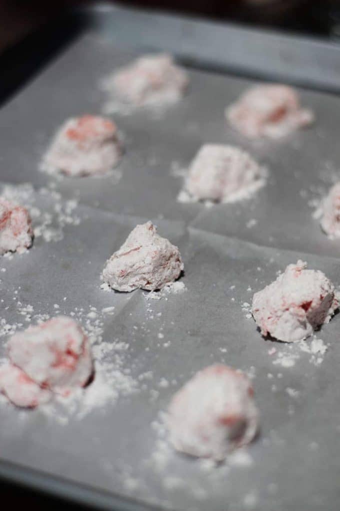 several balls of strawberry cake cookie dough rolled in powdered sugar on a prepared cookie sheet ready to be baked