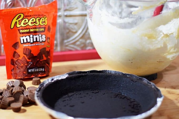 an oreo pie shell, a bag of mini reese\'s cups, and a large white mixing bowl of peanut butter pie filling