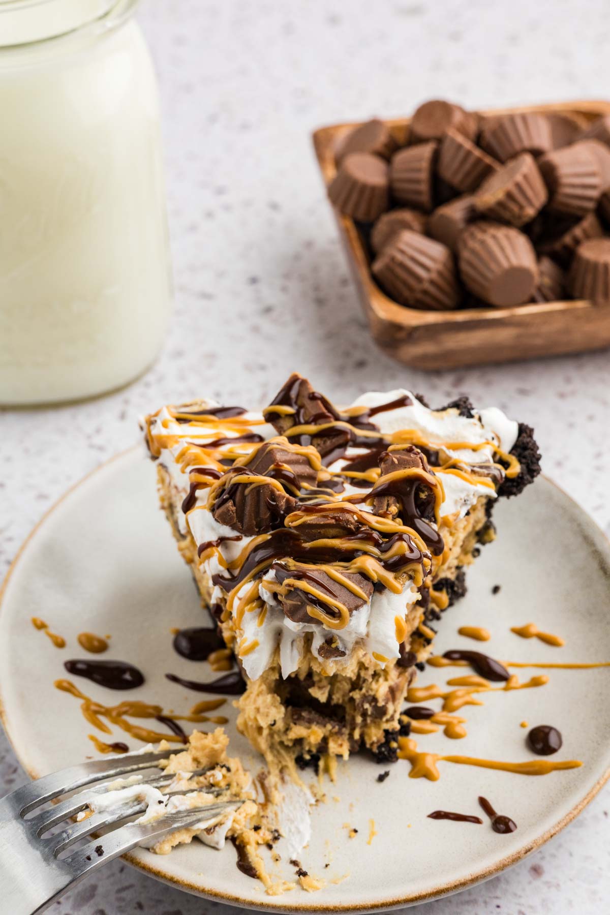 A slice of peanut butter pie topped with Reece's cups and drizzle with melted peanut butter and hot fudge.