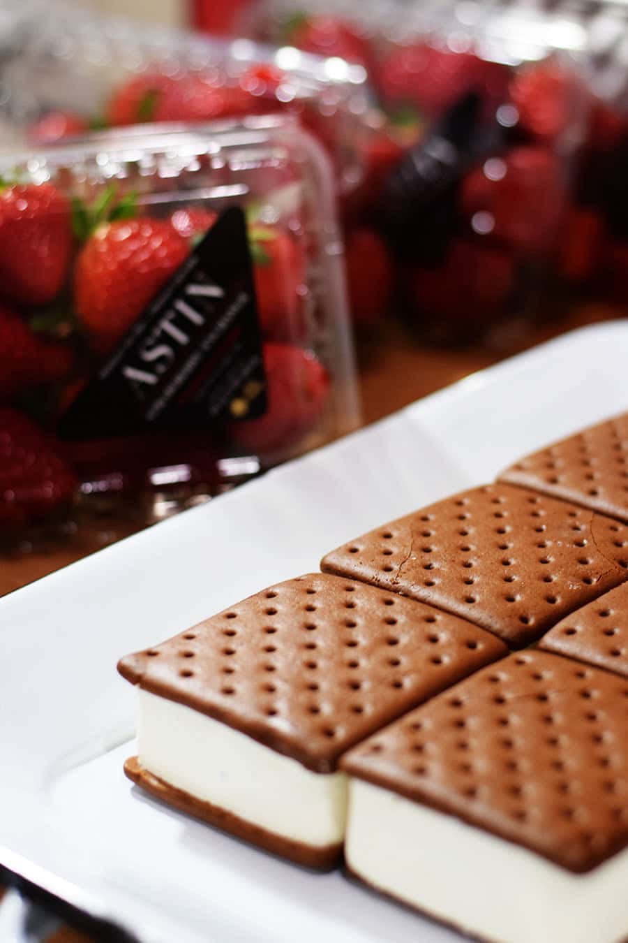 a side view of the ice cream sandwiches that comprise the first layer of this strawberry ice cream cake with a carton of strawberries in the background