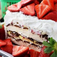 A close up of the midsection of this strawberry ice cream cake iced in whipped cream and topped with fresh strawberries