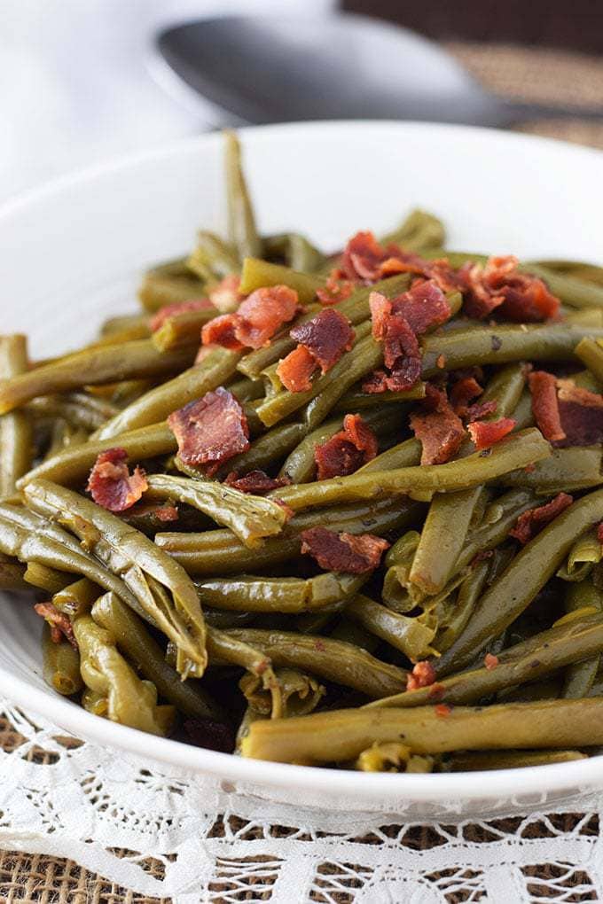 A white serving bowl filled with these southern-style green beans with crispy, crumbled bacon