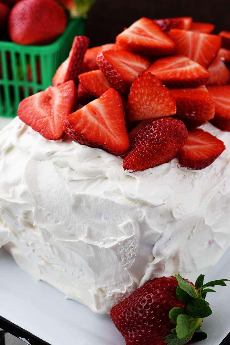 a closeup of this strawberry ice cream cake topped with fresh strawberries and whipped cream