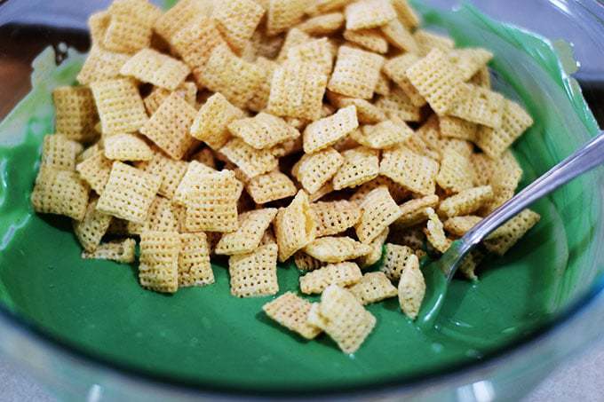Chex cereal in a bowl with a mixture of melted green candy melts, peanut butter and a bit of oil.