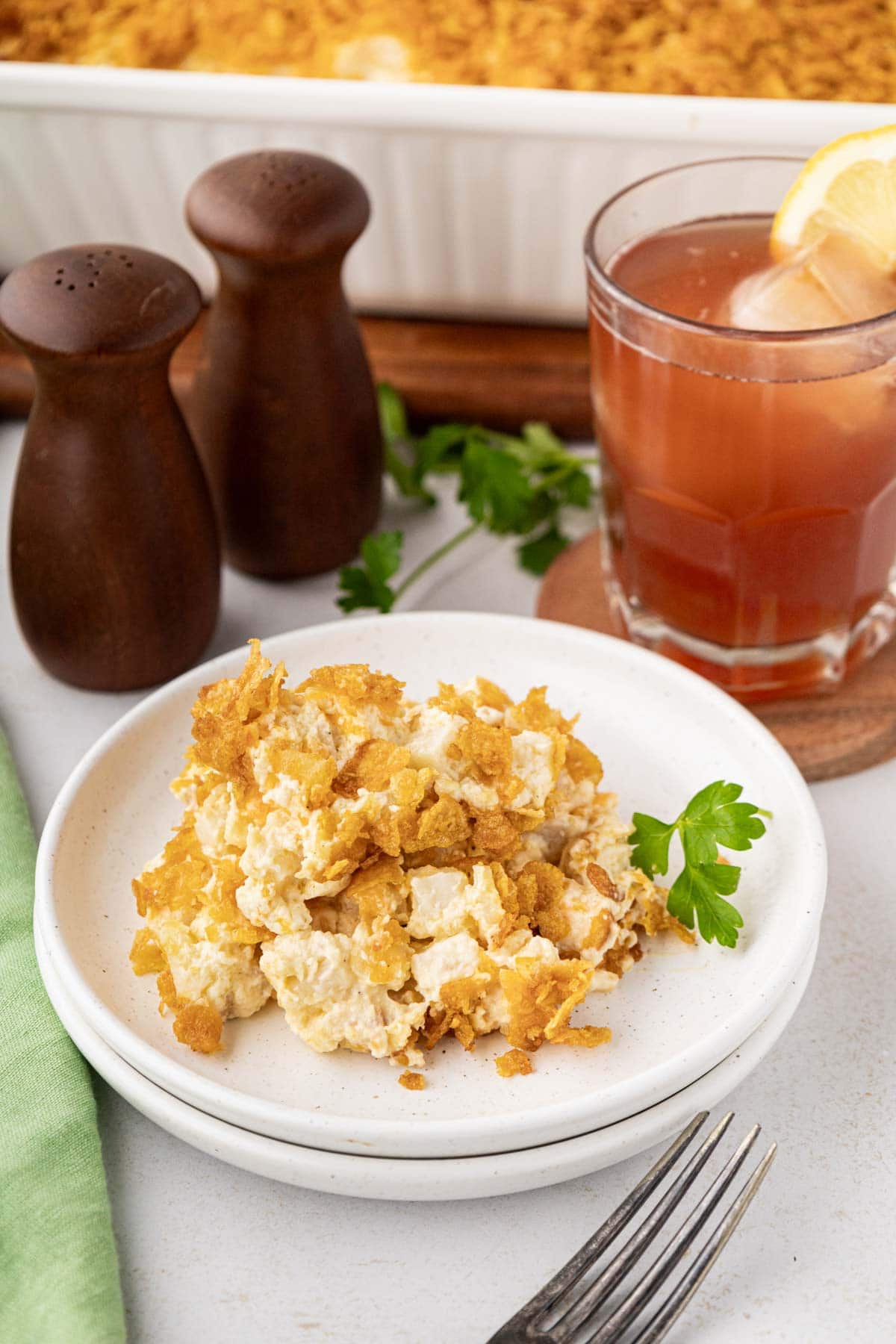 A serving of cheesy potato casserole on a white plate garnish with a parsley sprig.