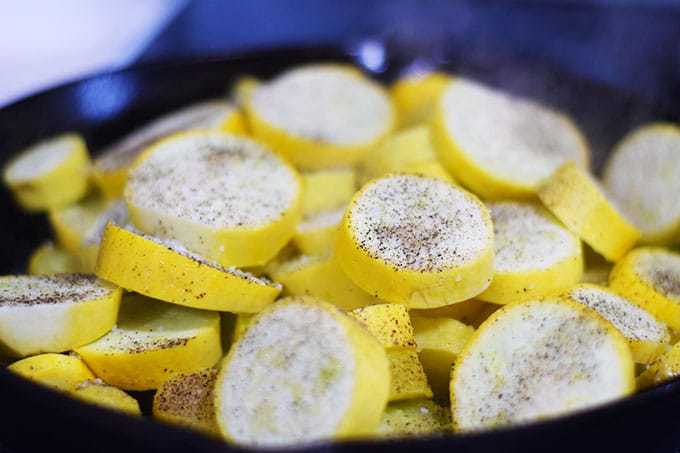 Yellow Squash frying in a cast iron skillet with salt and pepper on top