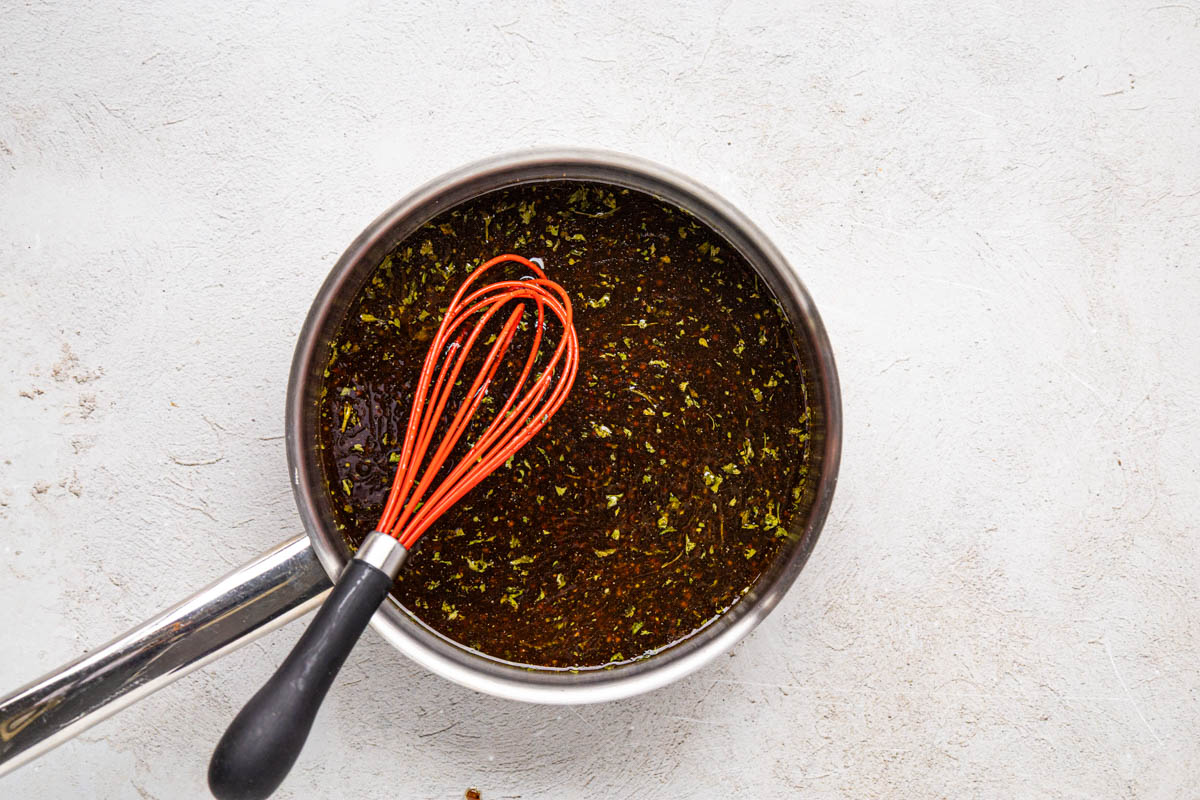 Cooking marinade in a sauce pan while stirring with a whisk.
