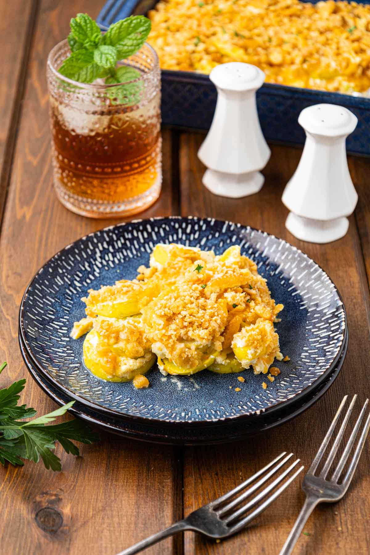 A plate of summer yellow squash casserole with a glass of tea in the background.