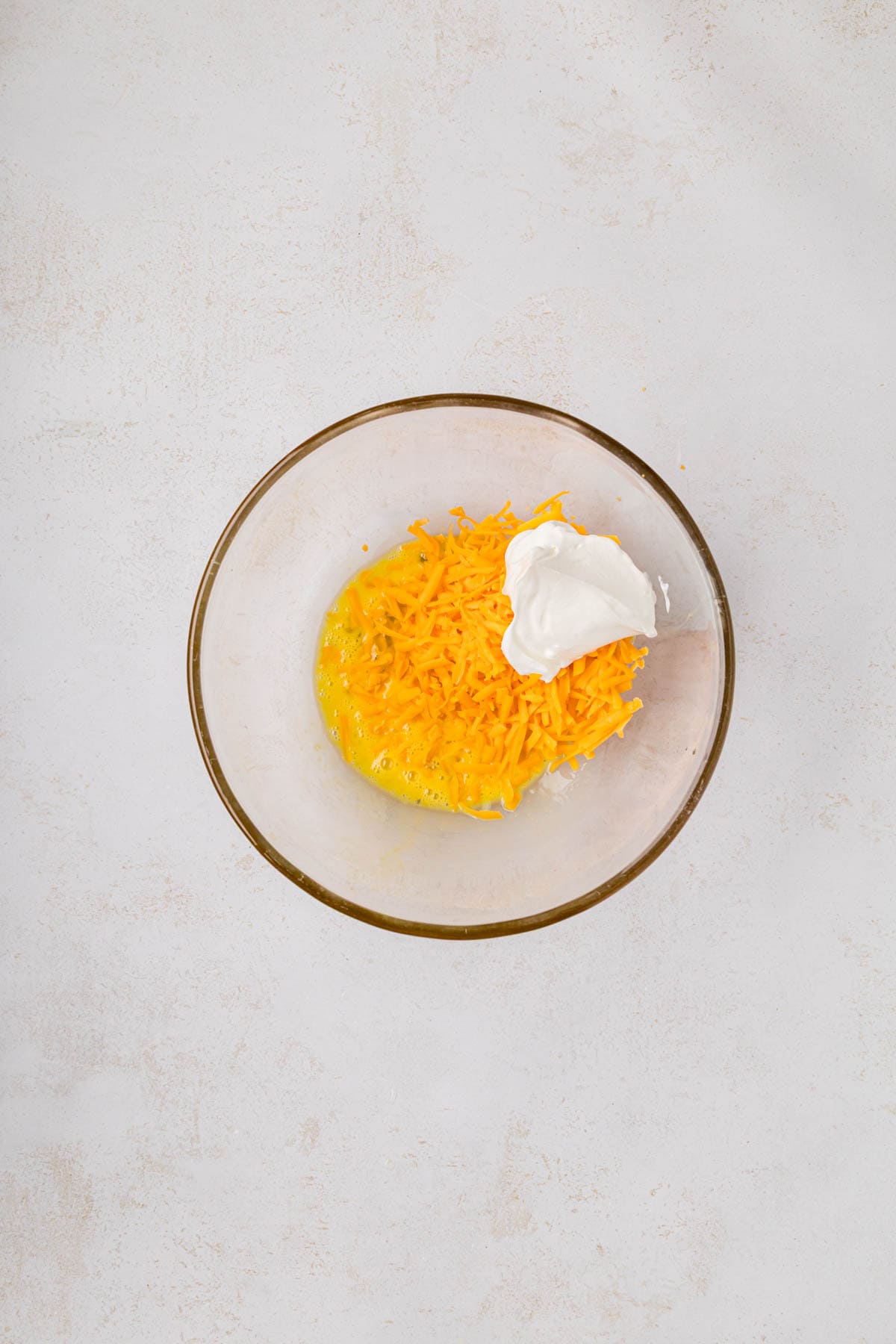 Shredded cheese and sour cream added to the bowl with eggs.