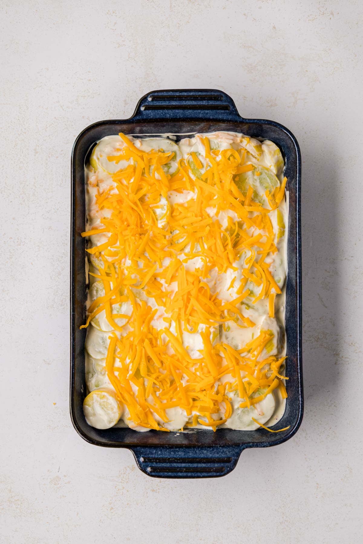 Squash mixture in the bottom of a baking dish with shredded cheese on top.