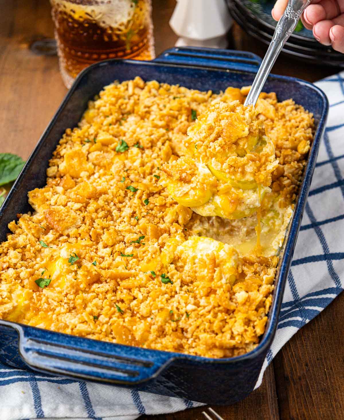 A cheesy squash casserole with a spoon taking a scoop out of the pan.