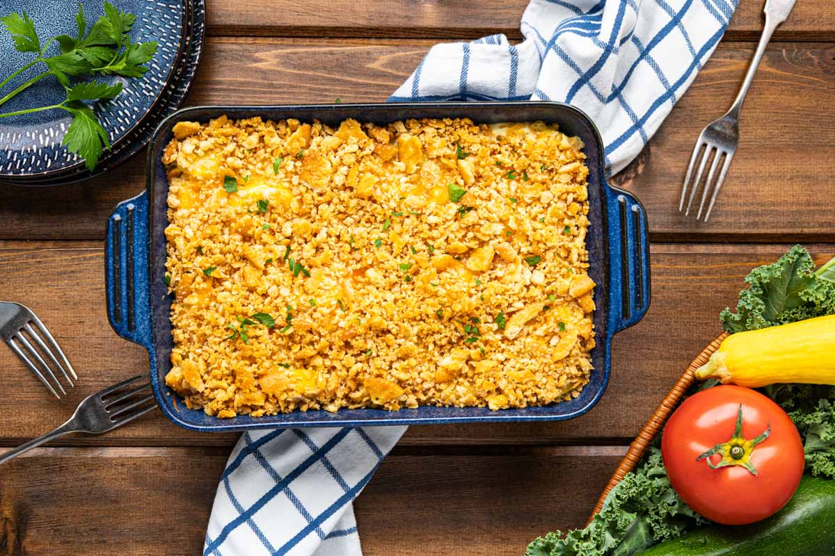A yellow summer squash casserole in a blue casserole dish on a wooden table.