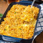 A cheesy yellow squash casserole with a spoon taking a scoop out of the pan.