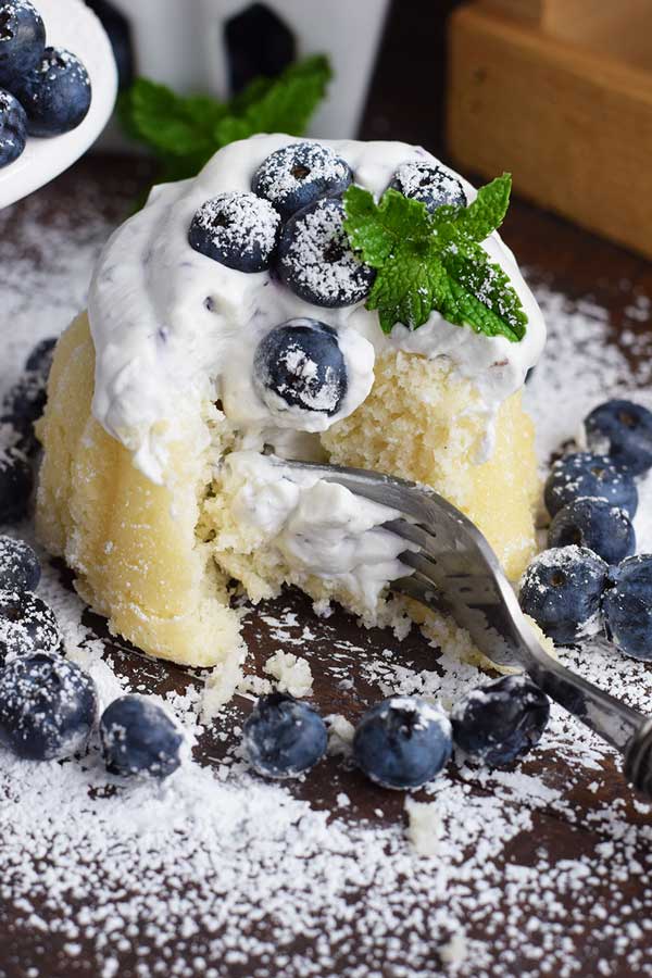 a fork taking a bite out of a mini almond bundt cake with blueberry whipped cream