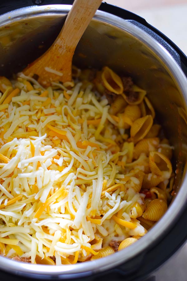 A close up of this instant pot cheesy taco pasta inside the pressure cooker with the shredded cheese on top being stirred in with a wooden spoon