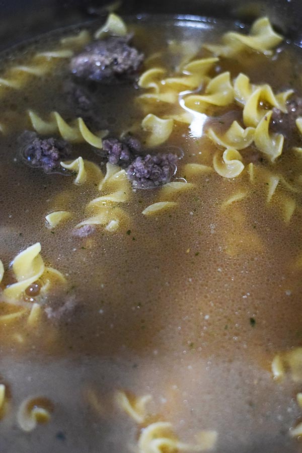 a closeup of this instant pot french onion ground beef and noodles recipe with broth, noodles, and ground beef