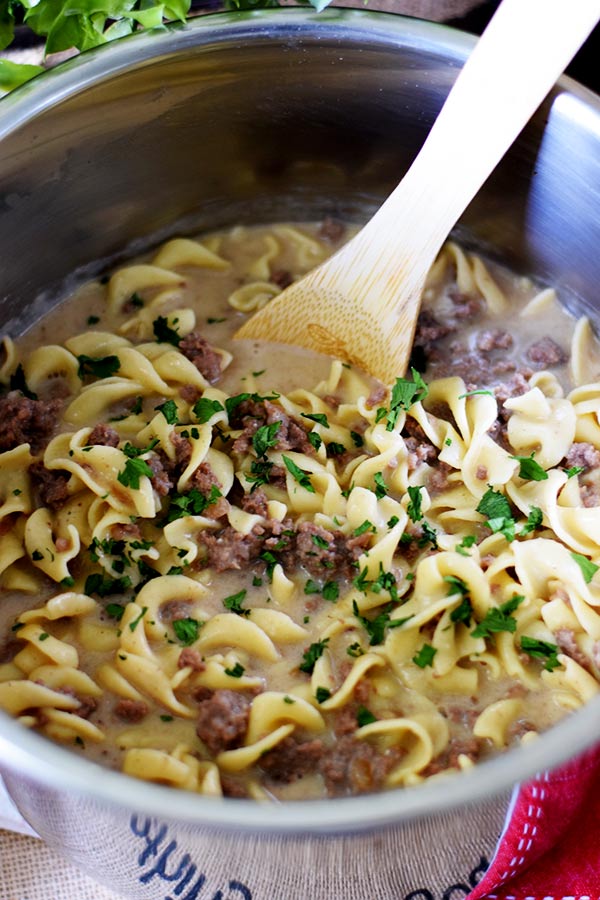 a closeup of this french onion ground beef and noodles recipe inside of the instant pot being stirred with a wooden spoon