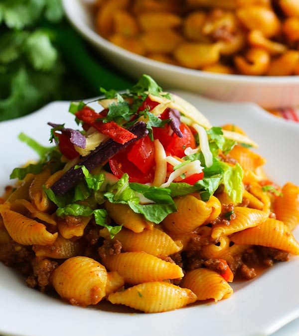 a serving of this instant pot taco pasta garnished with cilantro and tomatoes in a white bowl