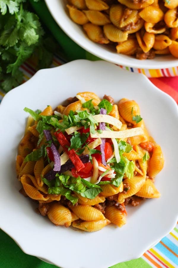 a serving of this instant pot taco pasta placed on a white plate and garnished with onions, cilantro, and tomatoes