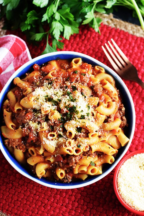 an overhead shot of a blue bowl filled with this instant pot goulash recipe garnished with parmesan cheese and chopped parsley and a fork off to the side