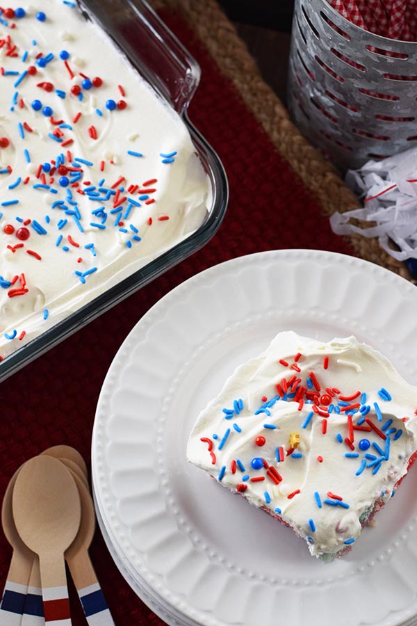 an overhead shot of a slice of this red, white, and blue poke cake with colorful fourth of july sprinkles