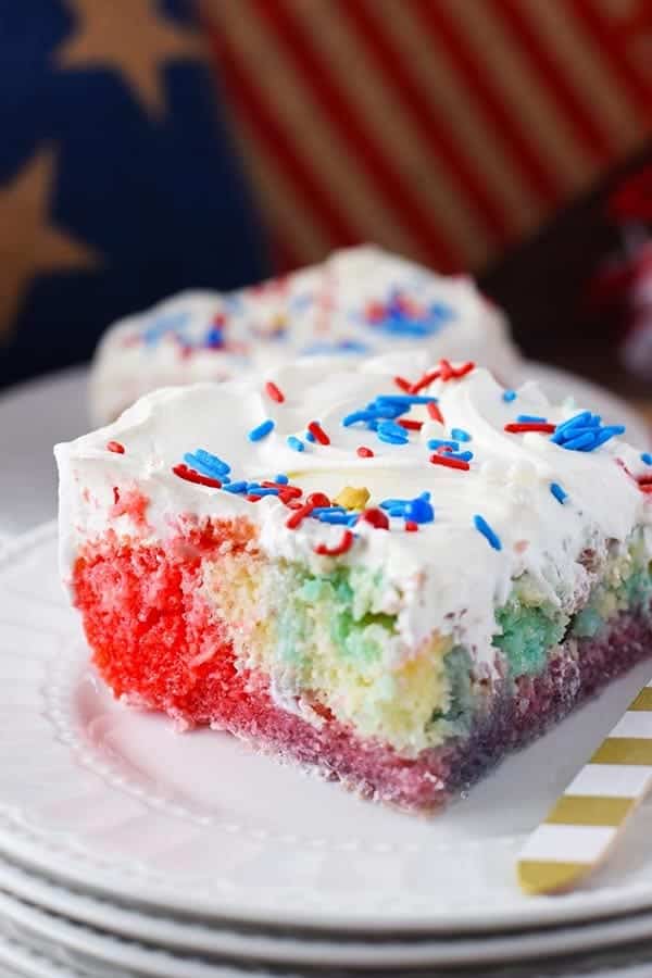 a slice of this red, white, and blue poke cake with whipped topping and colorful sprinkles