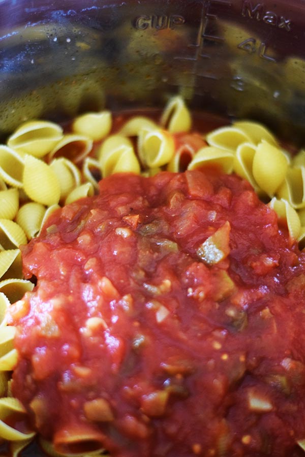 a closeup of mini pasta shells and red salsa in the pressure cooker to make this instant pot cheesy taco pasta recipe