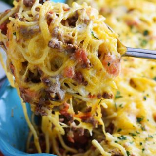 an closeup view of a forkful of this taco spaghetti bake topped with melted cheese and chopped parsley