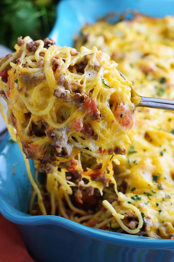 an closeup view of a forkful of this taco spaghetti bake topped with melted cheese and chopped parsley