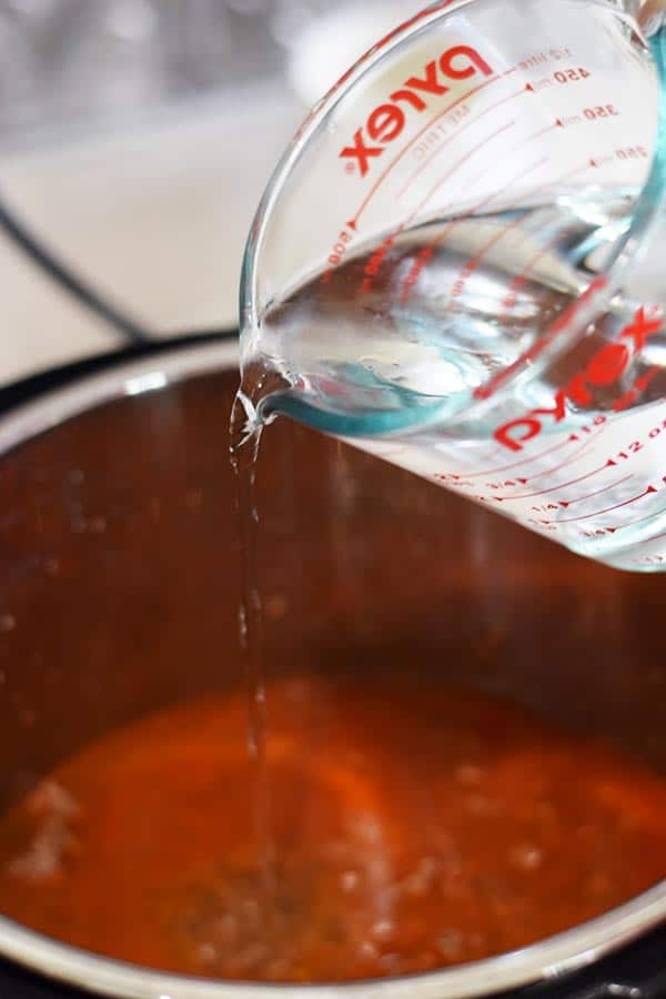 a glass measuring cup pouring water into the instant pot to make this cheesy taco pasta