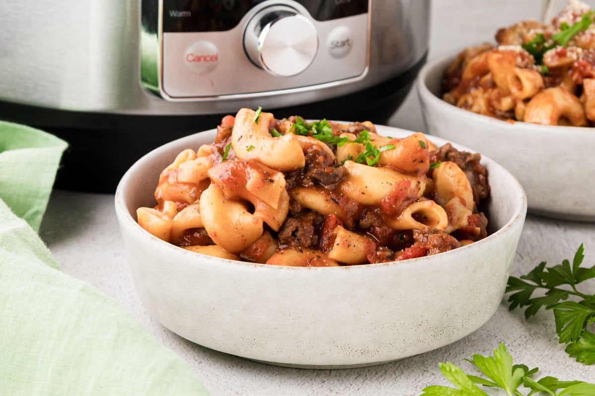A bowl of goulash made in an electric pressure cooker with the instant pot in the back ground.