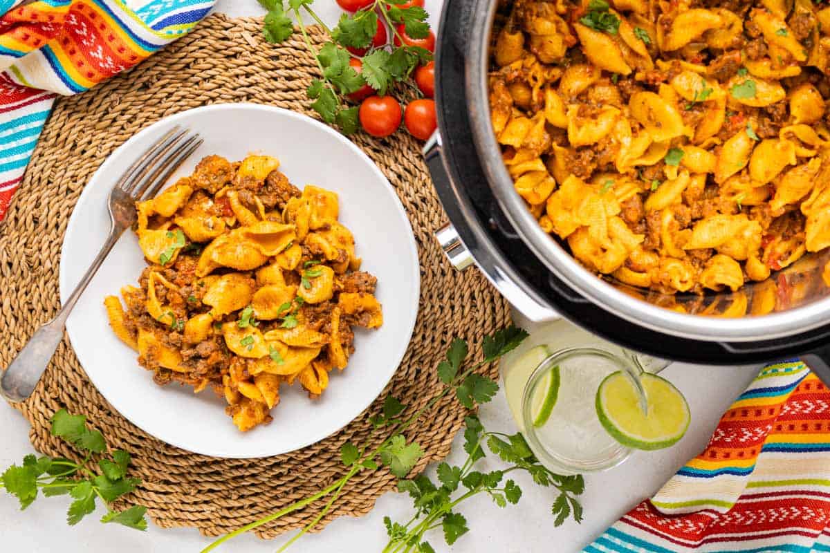 A table setting with a bowl of taco pasta and the instant pot beside it with the pasta inside.