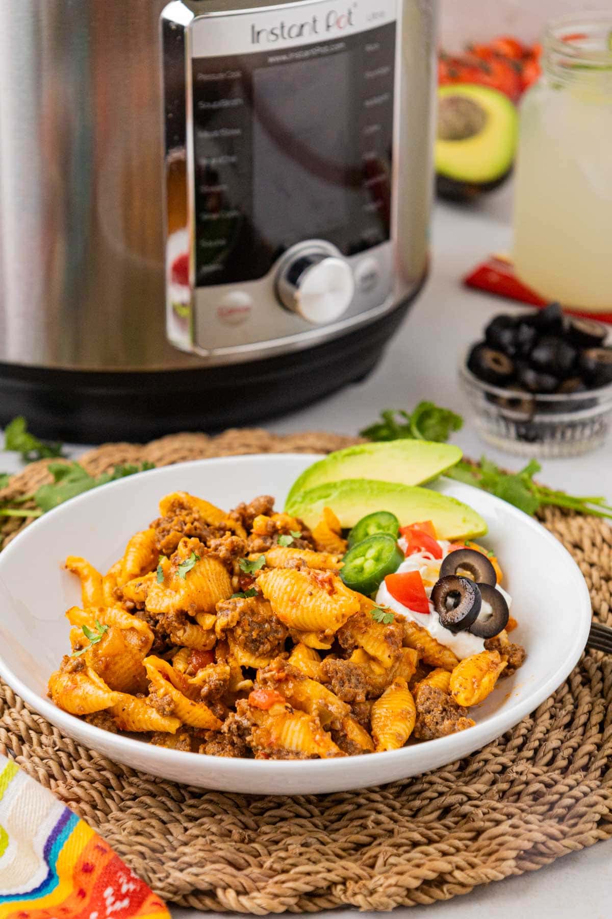A dinner bowl with cheesy taco pasta made in the instant pot garnished with avocado, sour cream and sliced jalapenos and black olives.