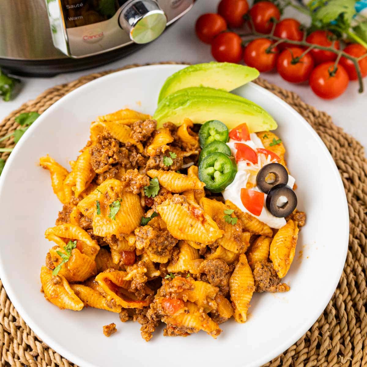A dinner bowl with cheesy taco pasta made in the instant pot garnished with avocado, sour cream and sliced jalapenos and black olives.