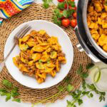 A table setting with a bowl of taco pasta and the instant pot beside it with the pasta inside.
