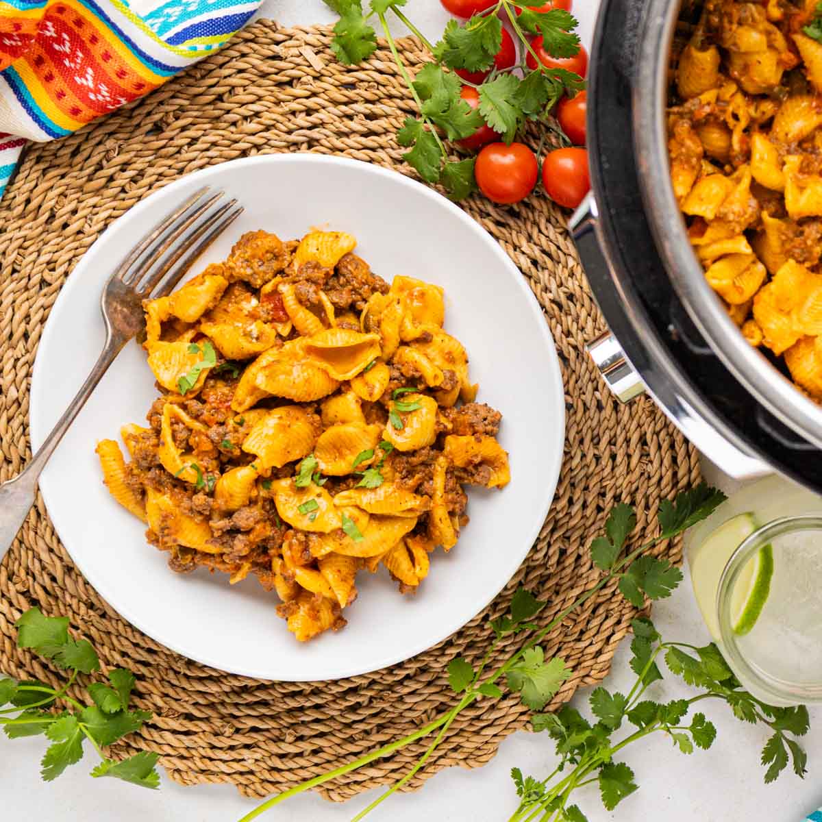 A table setting with a bowl of taco pasta and the instant pot beside it with the pasta inside.
