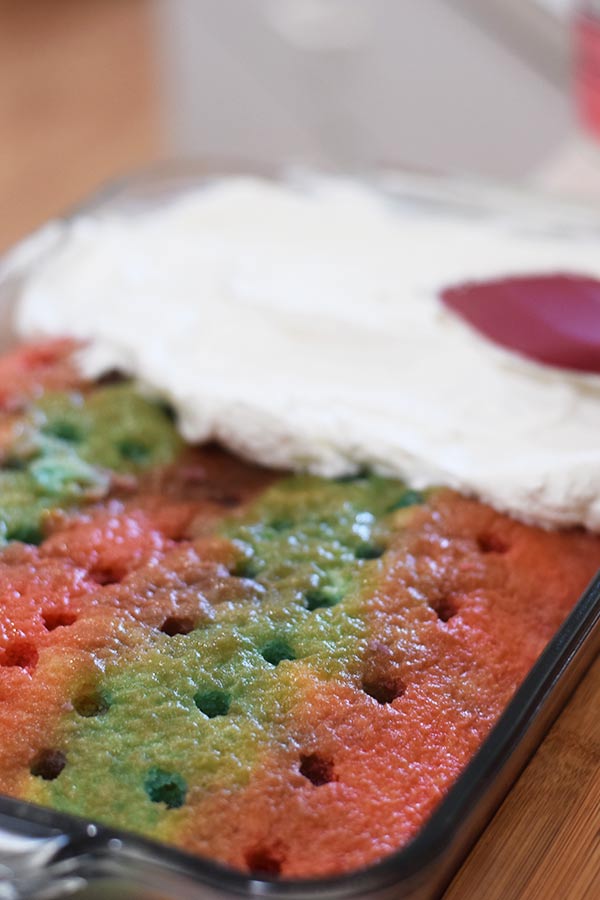 this red, white, and blue poke cake with holes in it and a whipped topping being spread across the top of it