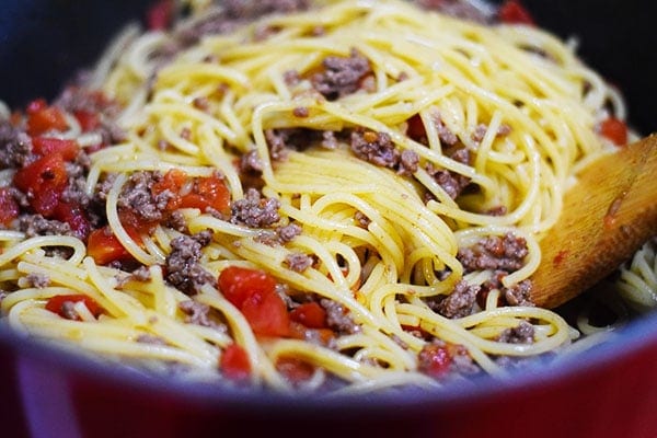 a close up of the spaghetti noodles, tomatoes, and ground beef in a pot for this baked taco spaghetti recipe