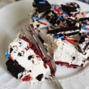 A slice of a no bake fireworks oreo cheesecake bar with red, white, and blue sprinkles and chopped oreos on top with a fork breaking off one bite