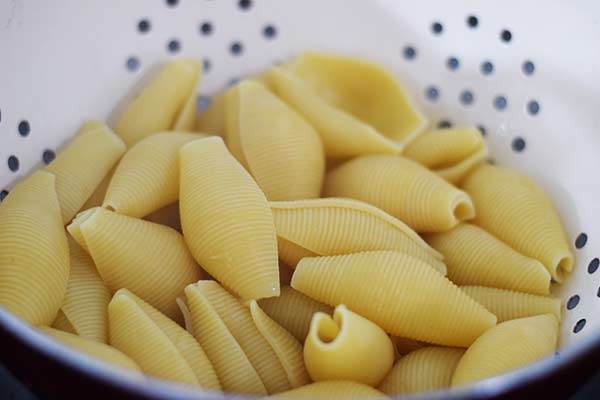 a close up of cooked jumbo pasta shells in a colander for this easy baked stuffed shells recipe