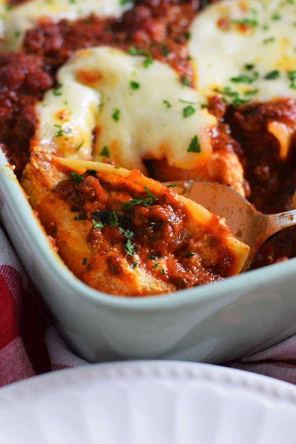 Spoon of Easy Baked Stuffed Shells out of a baking dish