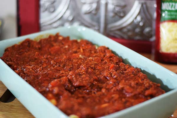 an overhead shot of the final layer of marinara sauce over a baking dish filled with these easy baked shells 