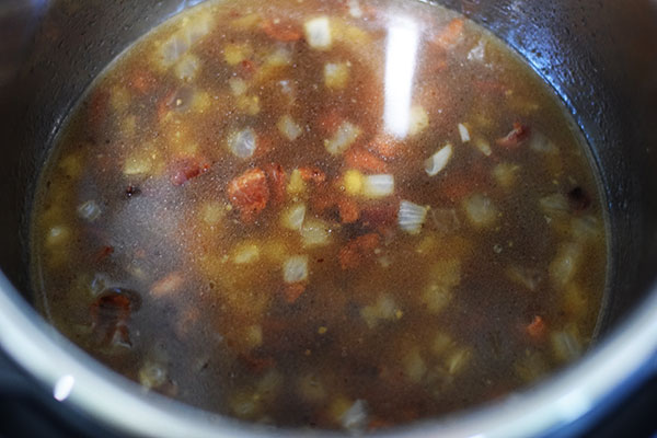 An overhead shot of the broth, onions, and bacon used to cook these southern-style green beans in the instant pot