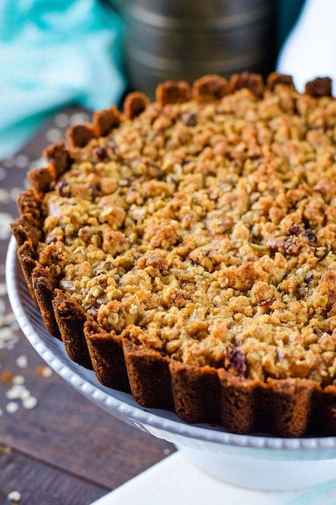 a close up of this apple butter cheesecake tart with a streusel topping on a cake stand for serving