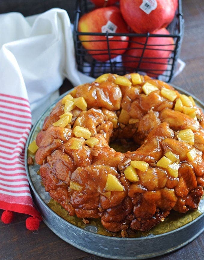 An overhead shot of this apple butter pecan sticky bun bites turned out of the bundt pan on a galvanized metal serving platter with a basket of apples in the background