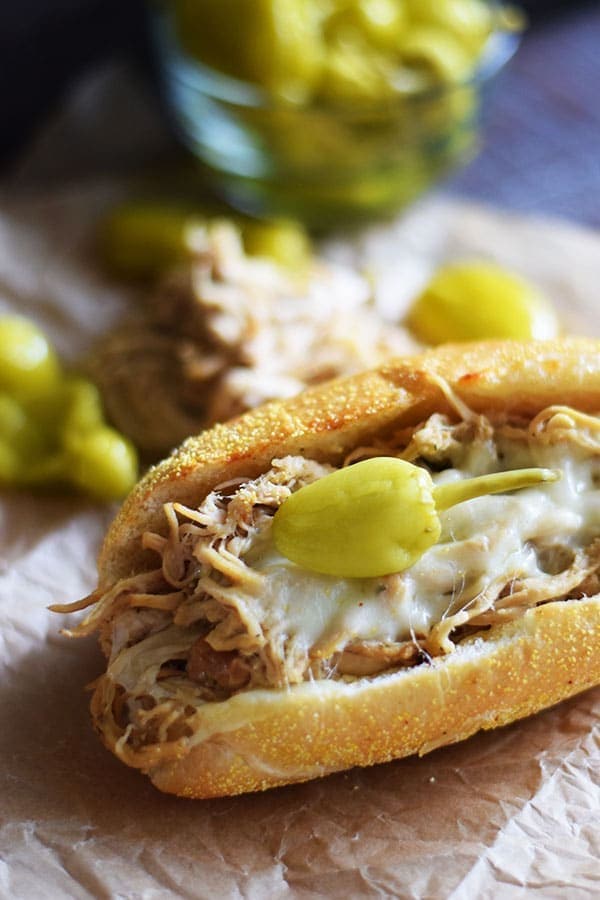 a close up of this crock pot Mississippi chicken sandwich topped with cheese and a banana pepper